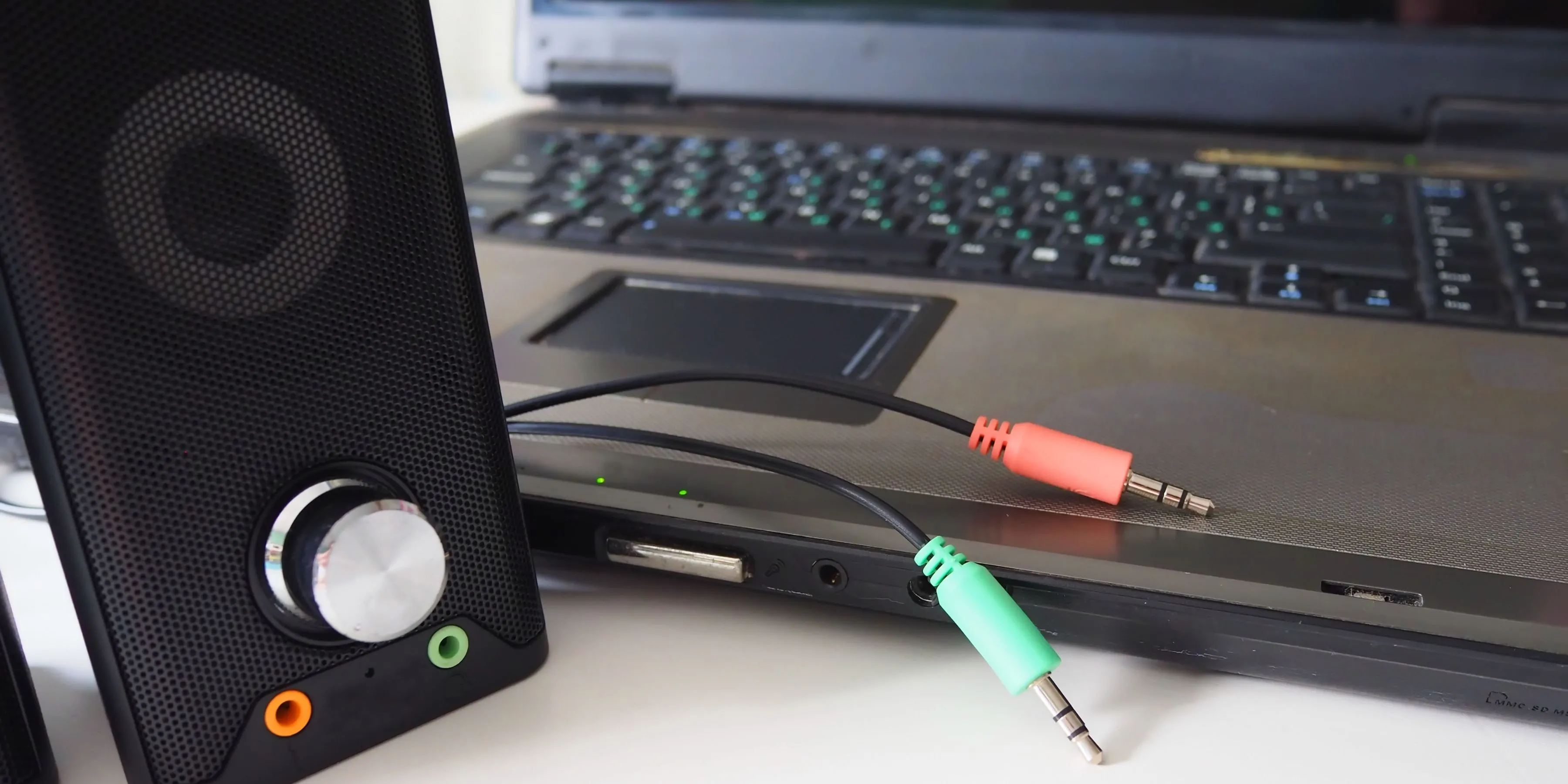 Hình ảnh một chiếc loa với các dây cáp âm thanh 3.5mm nằm cạnh một bộ PC, minh họa sự phức tạp của việc kết nối nhiều thiết bị ngoại vi.